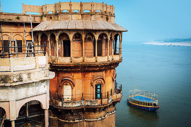 An ancient orange riverside temple structure towers over the Ganges with a small boat nearby, capturing timeless Indian architecture and serene waters by the sacred city of Varanasi.