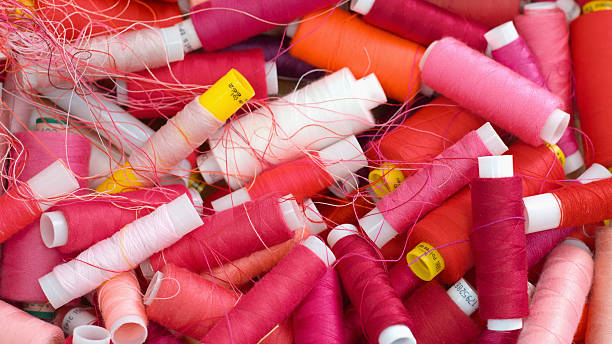 Assorted spools of vibrant red and pink sewing threads creating a textured background