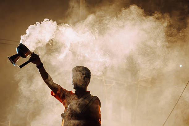 Varanasi, India - November 3, 2024: A man raises a ceremonial torch amid smoky illumination during a fire ceremony at a Hindu festival in Varanasi, capturing ritual energy, devotion, and dramatic atmosphere.