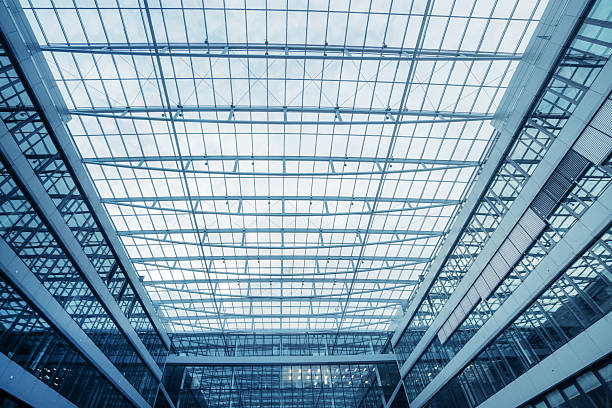 A vast, futuristic glass atrium with a skylight roof creates a cool, blue-toned interior. Modern architecture, open space, and symmetry convey efficiency and travel ambience in a contemporary airport setting.