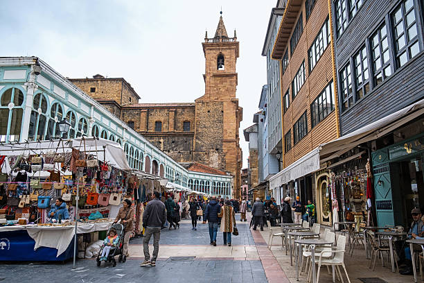 Oviedo, Spain - May 13, 2025. A busy day at the Mercado El Fontan market in El Fontan Square in Oviedo, Spain, with the Church of San Isidoro el Real visible in the background.