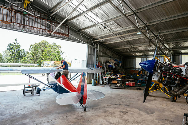 Airfield with hangar filled with private airplanes. Engineers and technicians working together  on private airplanes engine maitenance and repair