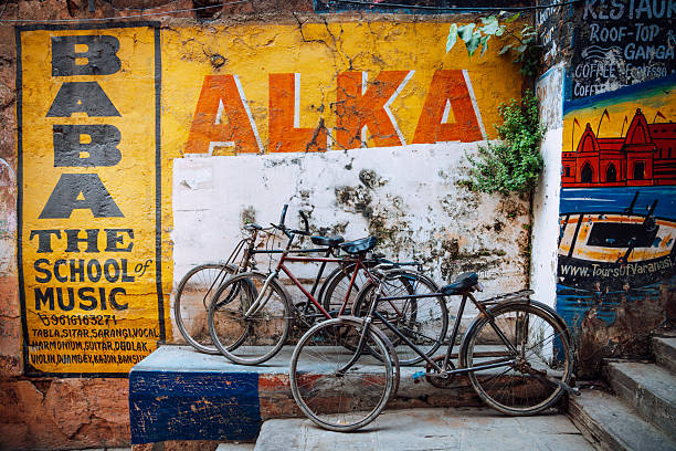 A vibrant wall mural in Varanasi features bold yellow and orange lettering with several bicycles parked in front, capturing an urban, nostalgic street scene in India.