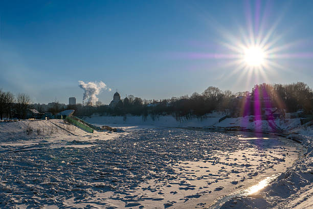 Winter landscape of the frozen Neris River flowing through Vilnius, Lithuania, illuminated by low winter sunlight. Snow-covered riverbanks, ice formations, and clear blue sky create a dramatic seasonal scene, ideal for climate, weather, travel, and urban winter concepts.