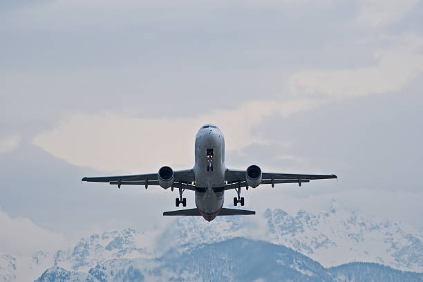White Plane Ascending Over Snow-Covered Mountains Under Overcast Sky