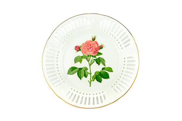 An elegant white porcelain plate features a hand-painted pink rose and an intricate pierced lattice border. The gold-rimmed antique dish is isolated on a white background, perfect for luxury decor.