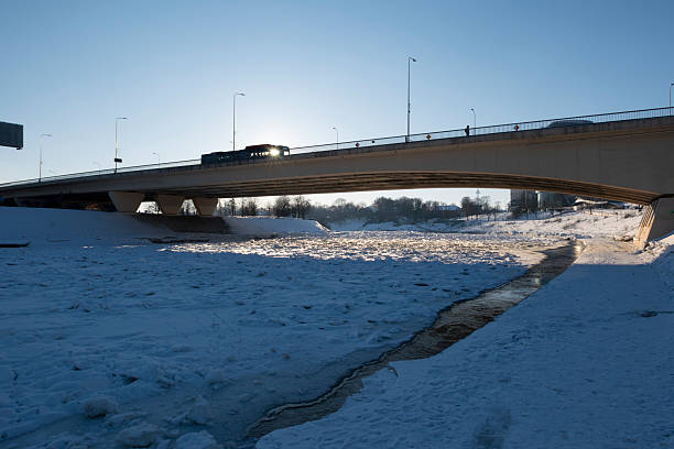 Winter cityscape of Vilnius, Lithuania, featuring the frozen Neris River and a modern urban skyline under clear blue sky. Snow-covered ice formations and contemporary architecture create a strong visual contrast, ideal for climate, winter weather, urban lifestyle, and European city concepts.