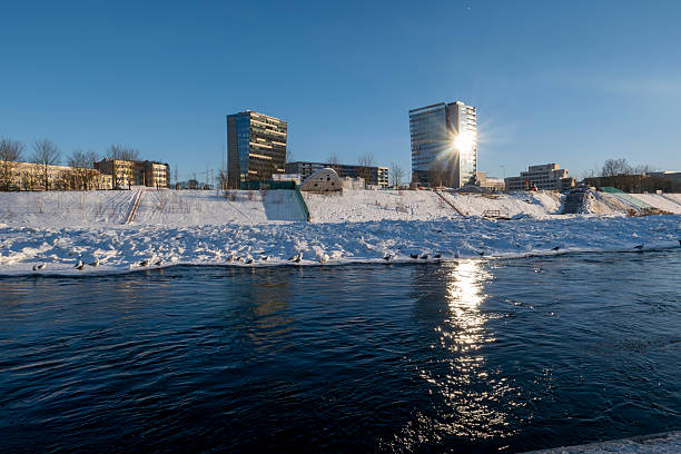 Winter cityscape of Vilnius, Lithuania, featuring the frozen Neris River and a modern urban skyline under clear blue sky. Snow-covered ice formations and contemporary architecture create a strong visual contrast, ideal for climate, winter weather, urban lifestyle, and European city concepts.