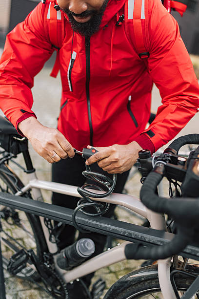 A focused man in a bright red jacket works on a bicycle lock, securing a bike with a key and tool. The scene conveys outdoor activity, cycling, repair work, and preparation for a ride, highlighting fitness, adventure, and initiative.