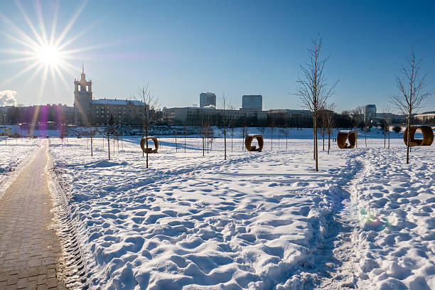 Winter cityscape of Vilnius, Lithuania, featuring the frozen Neris River and a modern urban skyline under clear blue sky. Snow-covered ice formations and contemporary architecture create a strong visual contrast, ideal for climate, winter weather, urban lifestyle, and European city concepts.