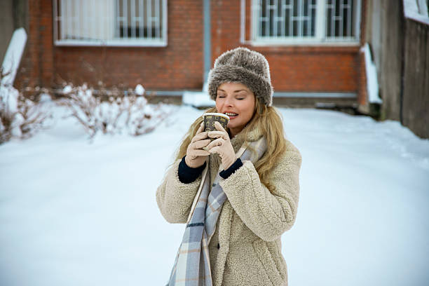 Woman in winter coat and fur hat drinking hot beverage