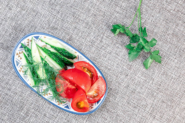 Slices of the fresh red tomato and green cucumber slices atop on a dish on a gray background