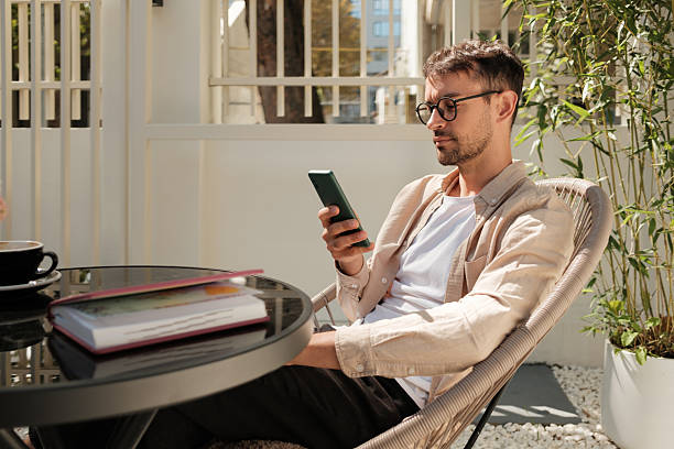 Relaxed man enjoying coffee outdoors while browsing smartphone