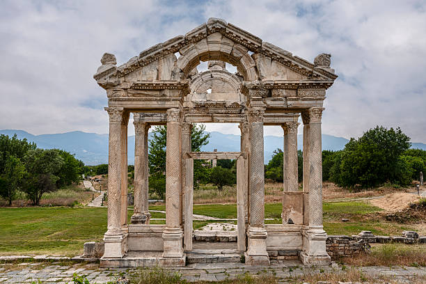 Four-columned gateway reveals elaborate architectural composition with Corinthian columns supporting ornate entablature at Aphrodisias tetrapylon, Turkey. The reconstructed monument shows characteristic Roman honorific architecture with the carefully restored elements demonstrating the original grandeur. The monumental tetrapylon represents the ceremonial entrance to the Temple of Aphrodite precinct, where visitors passed through this impressive gateway entering the goddess's sanctuary, with the elaborate architecture honoring Aphrodite and announcing the sacred nature of the space beyond this symbolic threshold between secular and sacred zones.