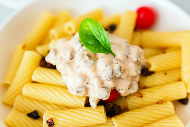 Raw italian pasta next to macaroni and spices on dark background