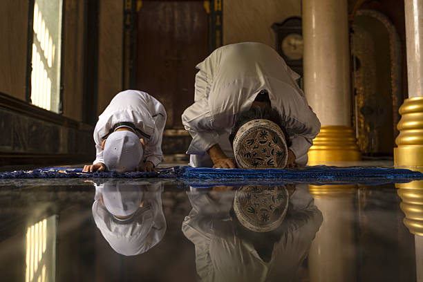 Heartwarming moment of a Muslim father guiding his little son during prayer time, teaching the values of faith, peace, and devotion in a sacred mosque setting.