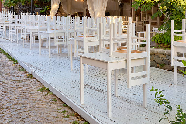 Empty outdoor cafe with upside down white chairs on wooden deck.