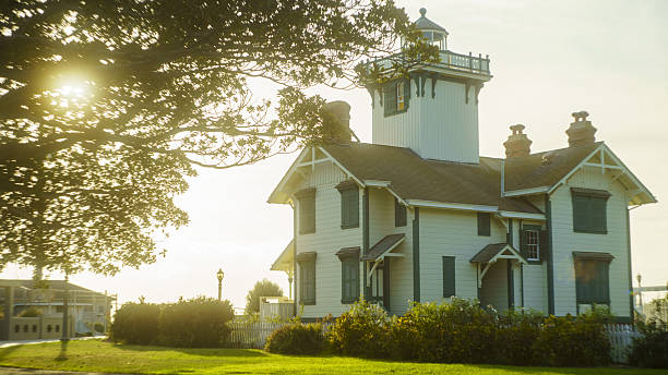 San Pedro, California, USA - April 25, 2023: A scenic view of the historic Victorian-style wooden Point Fermin Lighthouse during sunset. The image captures the elegant architectural details of the lighthouse with a bright sun flare shining through the trees in a coastal park in Los Angeles.