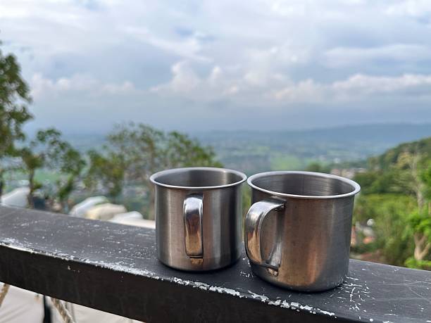 Two stainless steel mugs of hot coffee on a balcony