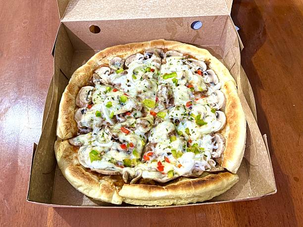 Freshly baked mushroom and green pepper pizza with melted cheese in a brown cardboard delivery box.