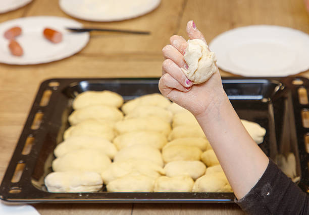 A hand is holding a piece of dough and pressing it into a pan. The dough is in the shape of a circle