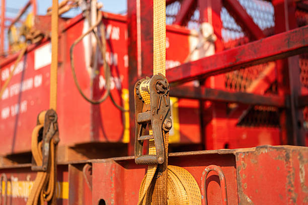 Latching belt strap with metal buckle that securing heavy load on trailer truck to prevent object falling during transportation. Close-up and selective focus.