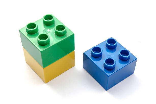 Two distinct groups of plastic construction toys, one stacked green and yellow, the other a single blue block, isolated on white