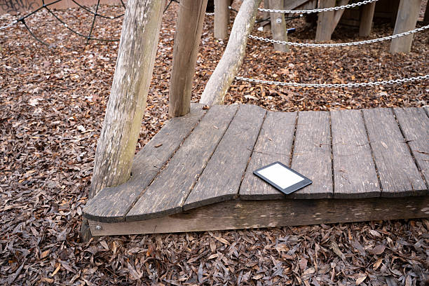 Ebook lying on a wooden playground structure outdoors. Everyday object in a casual setting, representing reading, learning, and leisure.