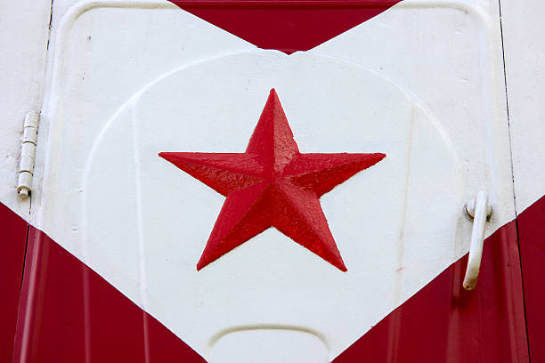 Close up of a red five pointed metal star attached to a painted steel door or industrial surface with white and red geometric background pattern.