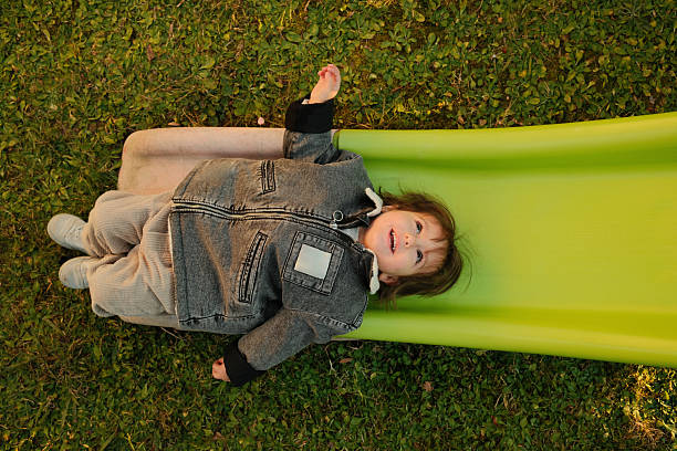 Child lying on back on a green slide in a park at sunset, enjoying playtime outdoors. Childhood joy concepts