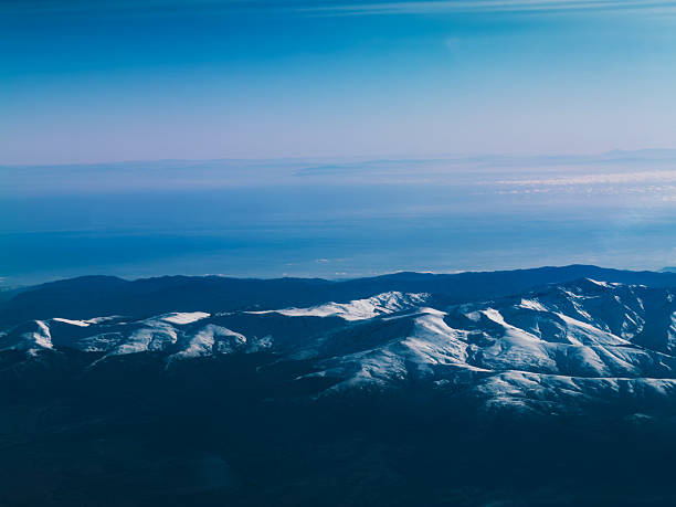 Aerial view of mountain range with snow capped peaks under clear blue sky. Concept of travel adventure, winter landscape and natural beauty.