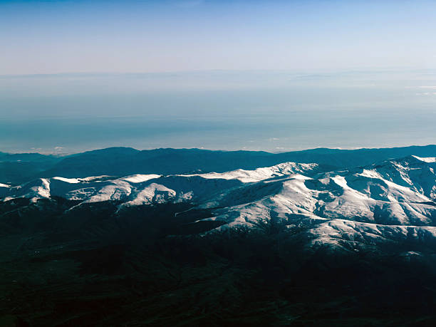 Aerial view of mountain range with snow capped peaks under clear blue sky. Concept of travel adventure, winter landscape and natural beauty.