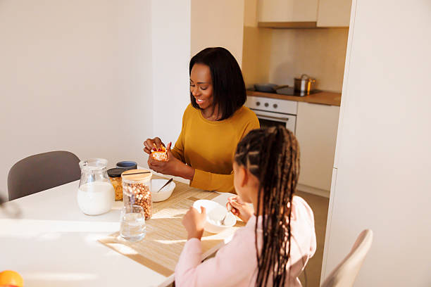 Mother peeling a tangerine while having breakfast with daughter at home
