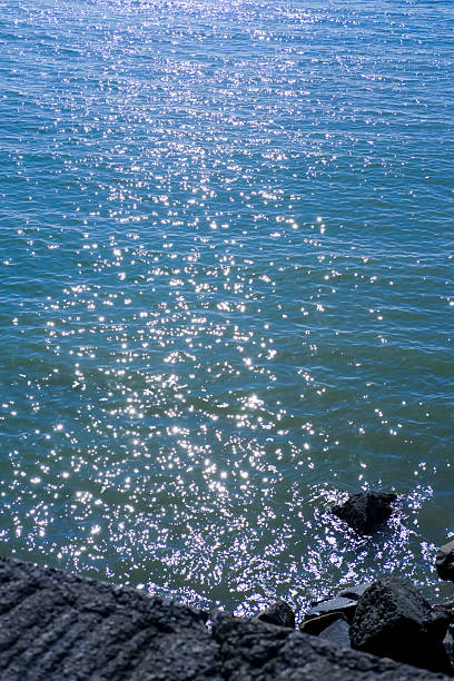 This image captures bright sunlight sparkling on gentle blue sea water, with small waves creating a shimmering pattern on the surface.