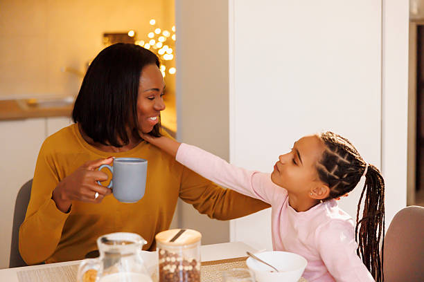 Beautiful mid adult mother drinking morning coffee while having a breakfast at home with her little daughter