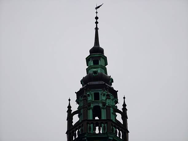 Ornate spire silhouetted against grey sky, showcasing verdigris copper details, finials and turrets, dramatic