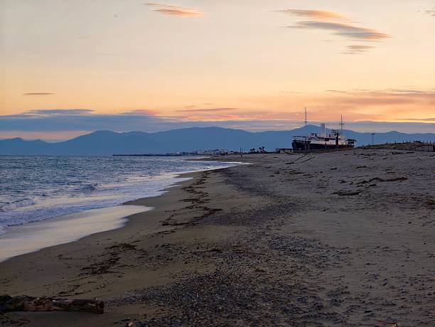 Sunset coastal harbor with moored boat, gentle surf and warm sky tones, quiet shoreline near low pier creating