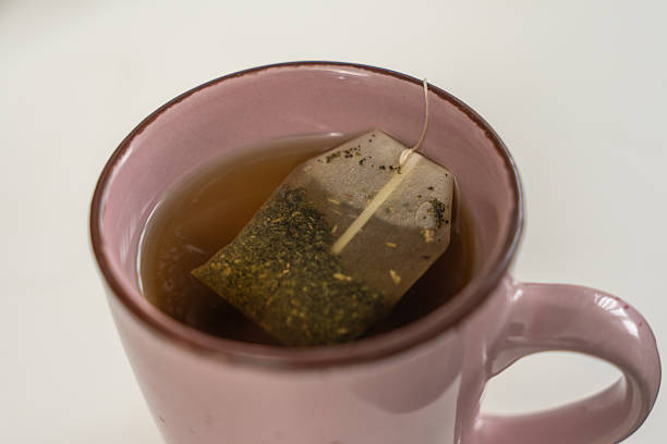 A tea bag is floating in a cup of tea. The tea bag is green and has a long stem