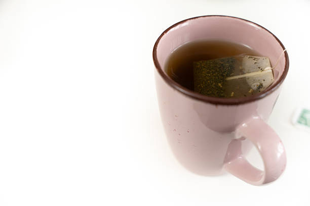 A pink mug with a tea bag in it. The tea bag is green and black. The mug is on a white surface