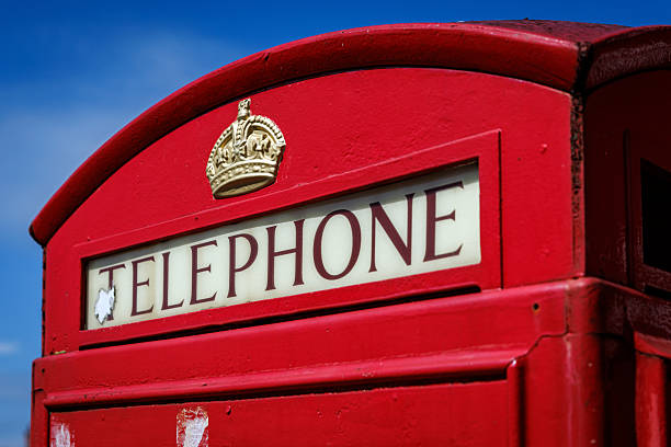 A close-up view of the sign on a classic red British telephone box with a crown emblem and blue sky.