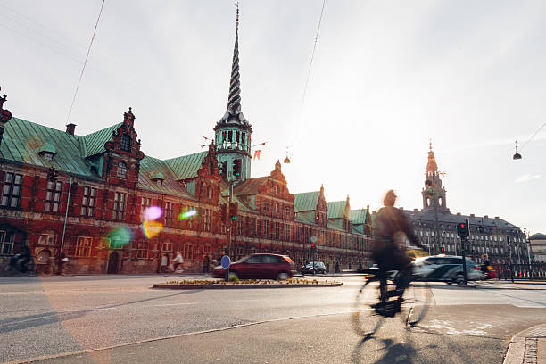 Daily life unfolds in Copenhagen as people walk, cycle, and commute through the city. Motion blur emphasizes the rhythm of urban living, with pedestrians and cyclists moving past historic architecture, bridges, and streets. The scene reflects sustainable transport, active lifestyles, and the calm efficiency of a modern European capital where movement is constant but unhurried.