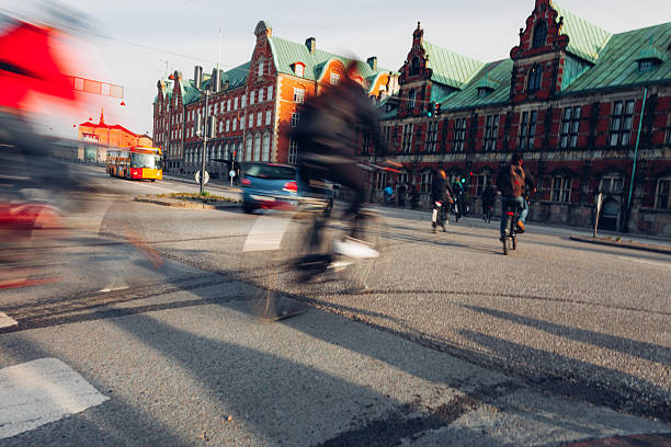 Daily life unfolds in Copenhagen as people walk, cycle, and commute through the city. Motion blur emphasizes the rhythm of urban living, with pedestrians and cyclists moving past historic architecture, bridges, and streets. The scene reflects sustainable transport, active lifestyles, and the calm efficiency of a modern European capital where movement is constant but unhurried.