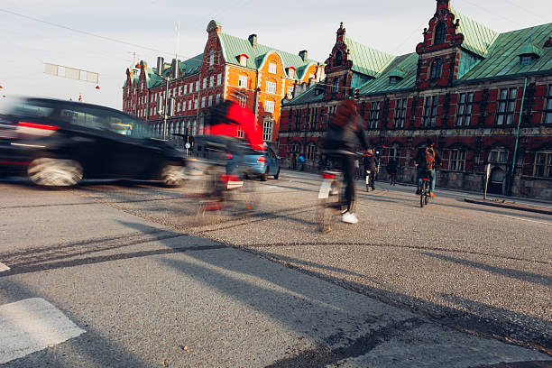 Daily life unfolds in Copenhagen as people walk, cycle, and commute through the city. Motion blur emphasizes the rhythm of urban living, with pedestrians and cyclists moving past historic architecture, bridges, and streets. The scene reflects sustainable transport, active lifestyles, and the calm efficiency of a modern European capital where movement is constant but unhurried.