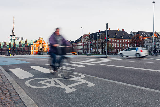 Daily life unfolds in Copenhagen as people walk, cycle, and commute through the city. Motion blur emphasizes the rhythm of urban living, with pedestrians and cyclists moving past historic architecture, bridges, and streets. The scene reflects sustainable transport, active lifestyles, and the calm efficiency of a modern European capital where movement is constant but unhurried.