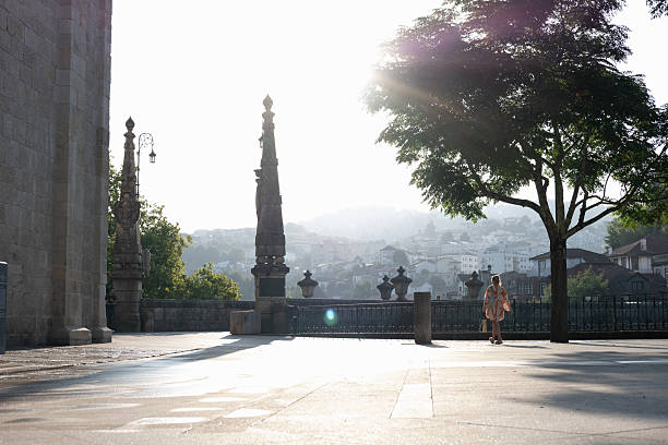 Amarante, portugal; august 27, 2024: woman walking on a historic square with sun flares and a city view