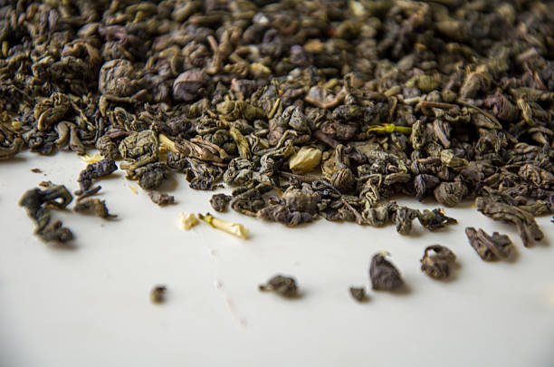 Close-up of loose dried green tea leaves scattered on a white surface, showing texture and detail for beverage or culinary use.