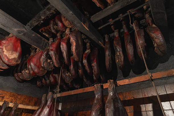 A rustic smokehouse scene showing rows of hanging cured meats inside a wooden interior. Evokes traditional food preservation, artisanal butchery, and homestyle charcuterie