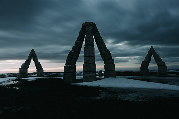 Arctic Henge stone monument standing prominently in Raufarhöfn, Iceland, against a dramatic twilight sky with snow on the dark ground, showcasing ancient Nordic and pagan mythology