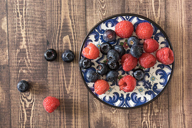 Blueberries and raspberries placed on a decorative plate and rustic wooden table