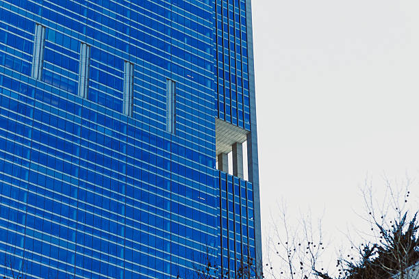 A tall building with a blue glass exterior features a unique cut-out section. This structure stands in an urban location beneath a cloudy sky.
